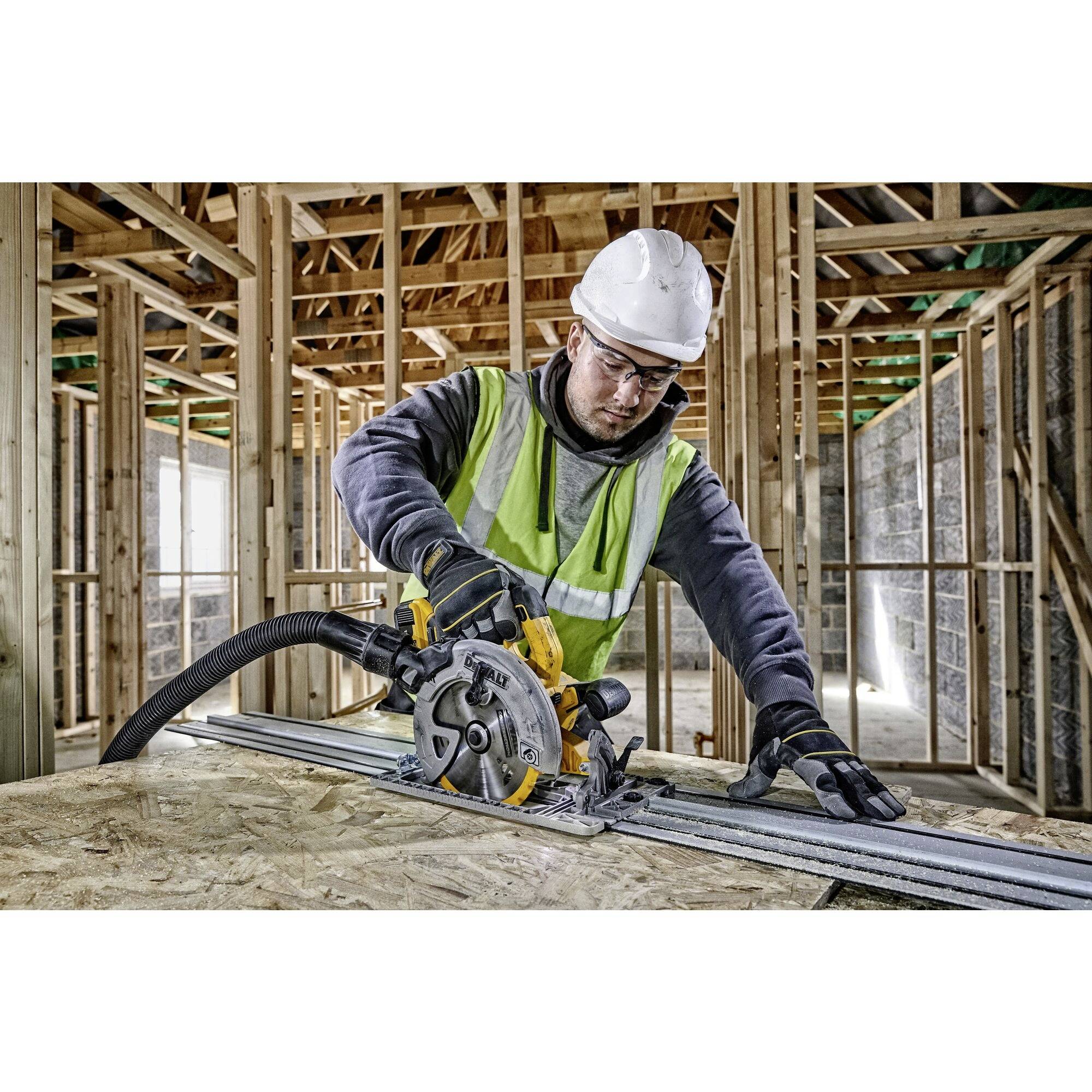 A construction worker wearing a hard hat and safety glasses is cutting wood with a circular saw in a partially completed building.