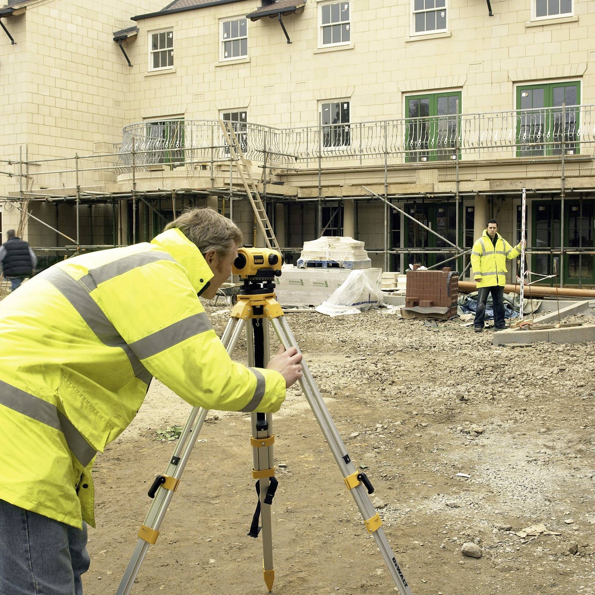 Construction workers are using a surveying instrument in front of a building under construction, surrounded by scaffolding.