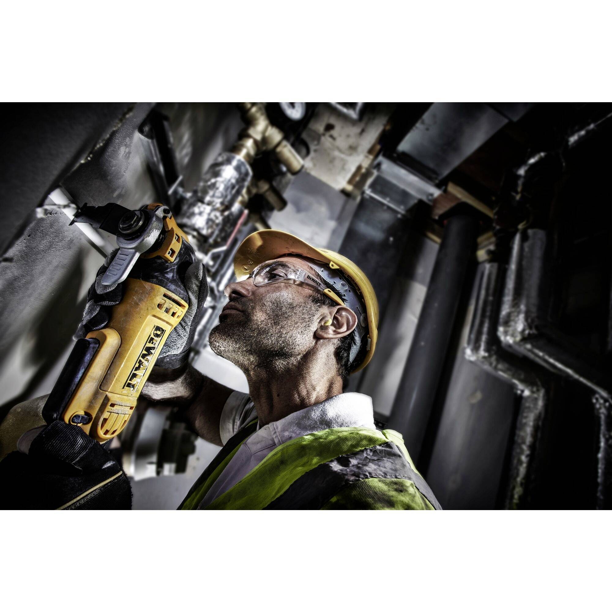 'A worker wearing a hard hat and safety glasses uses an electric tool on a wall. He is wearing a high-visibility vest. Working in a technical environment.'