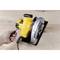 A hand is operating a screwdriver to secure the blade of a yellow circular saw on a wooden table.