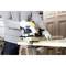 A person is sawing through a wooden board with an electric circular handsaw. They are wearing gloves and the saw is yellow and black.