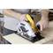 A man is cutting a wooden board with an electric circular saw. He is wearing casual clothing and working in a workshop environment.