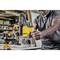 A person is using a yellow router to perform precise woodworking in a workshop. Tools are visible in the background.