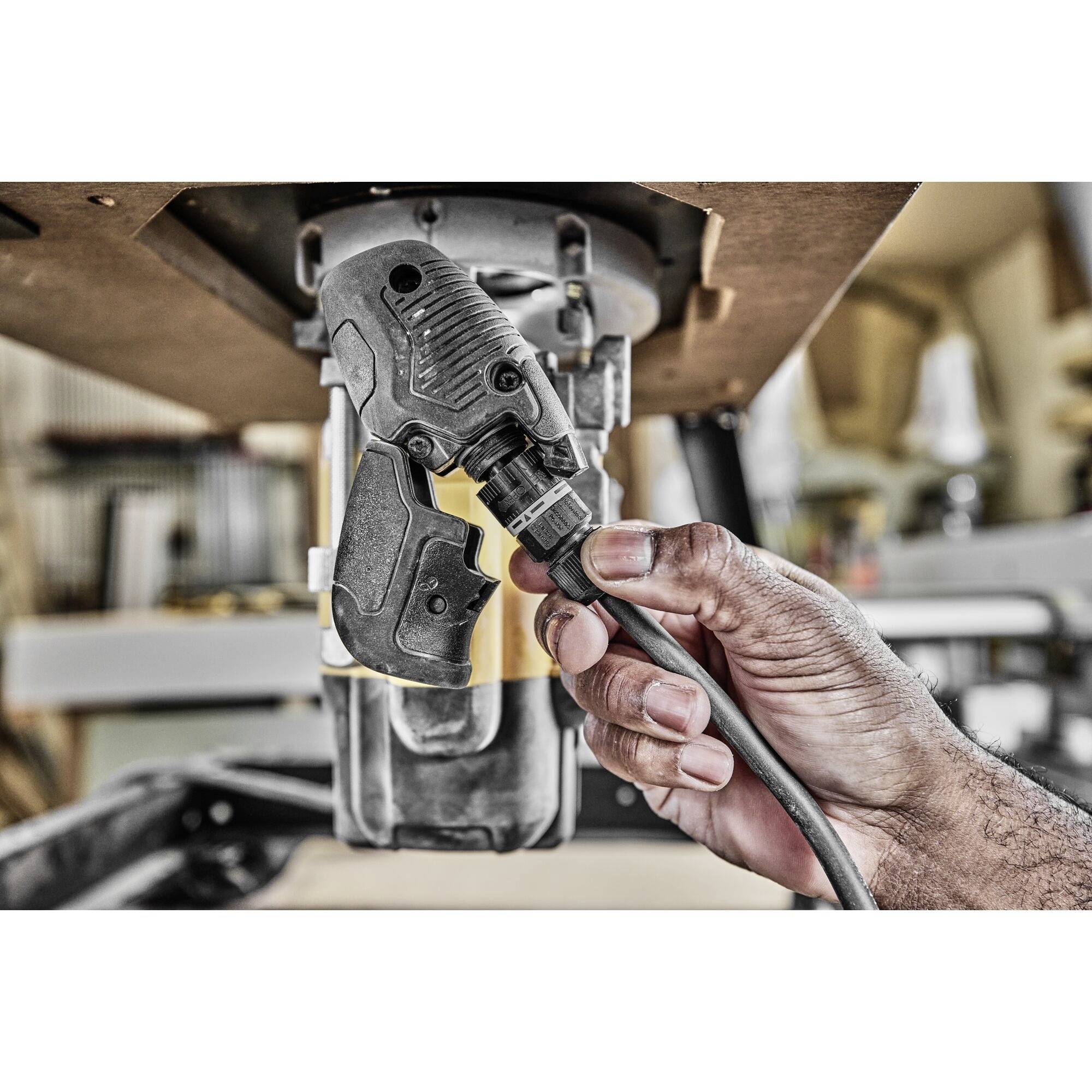 A person is holding a drill, plugging in a cable and preparing to work. In a workshop environment.
