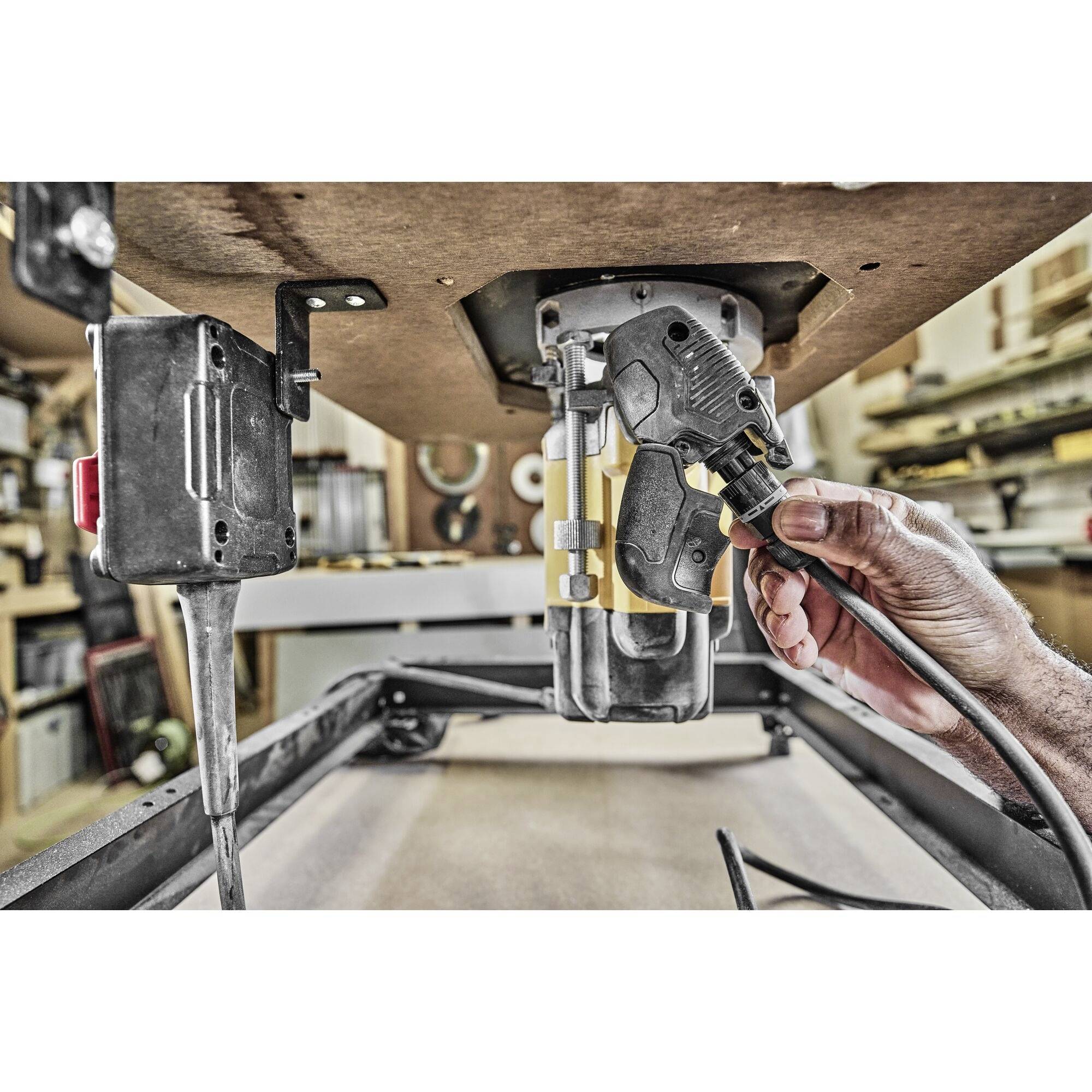A hand is holding an electric saw tool in a workshop. Workbenches and tools can be seen in the background.