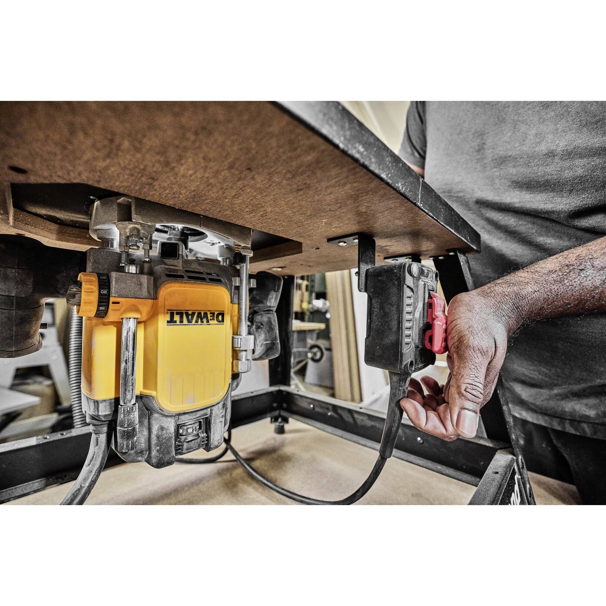 A person switches on a yellow and black machine tool underneath a table. They use a red switch on the black cable.