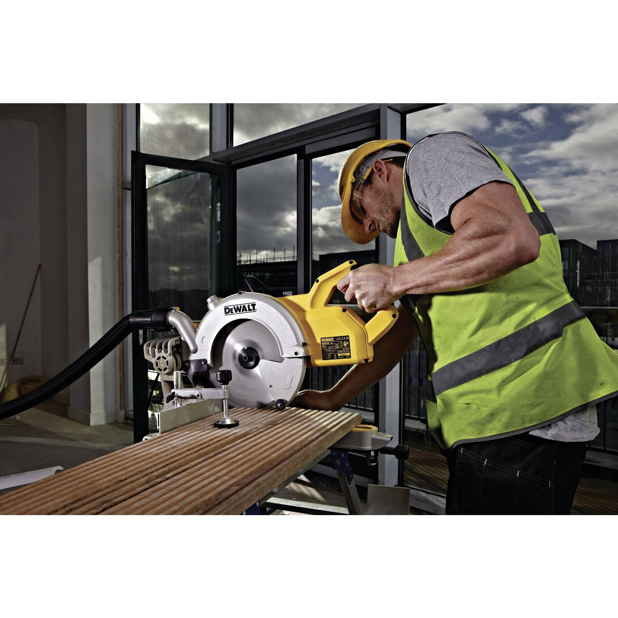 A person in protective clothing is sawing a wooden board with a circular saw in a workshop.