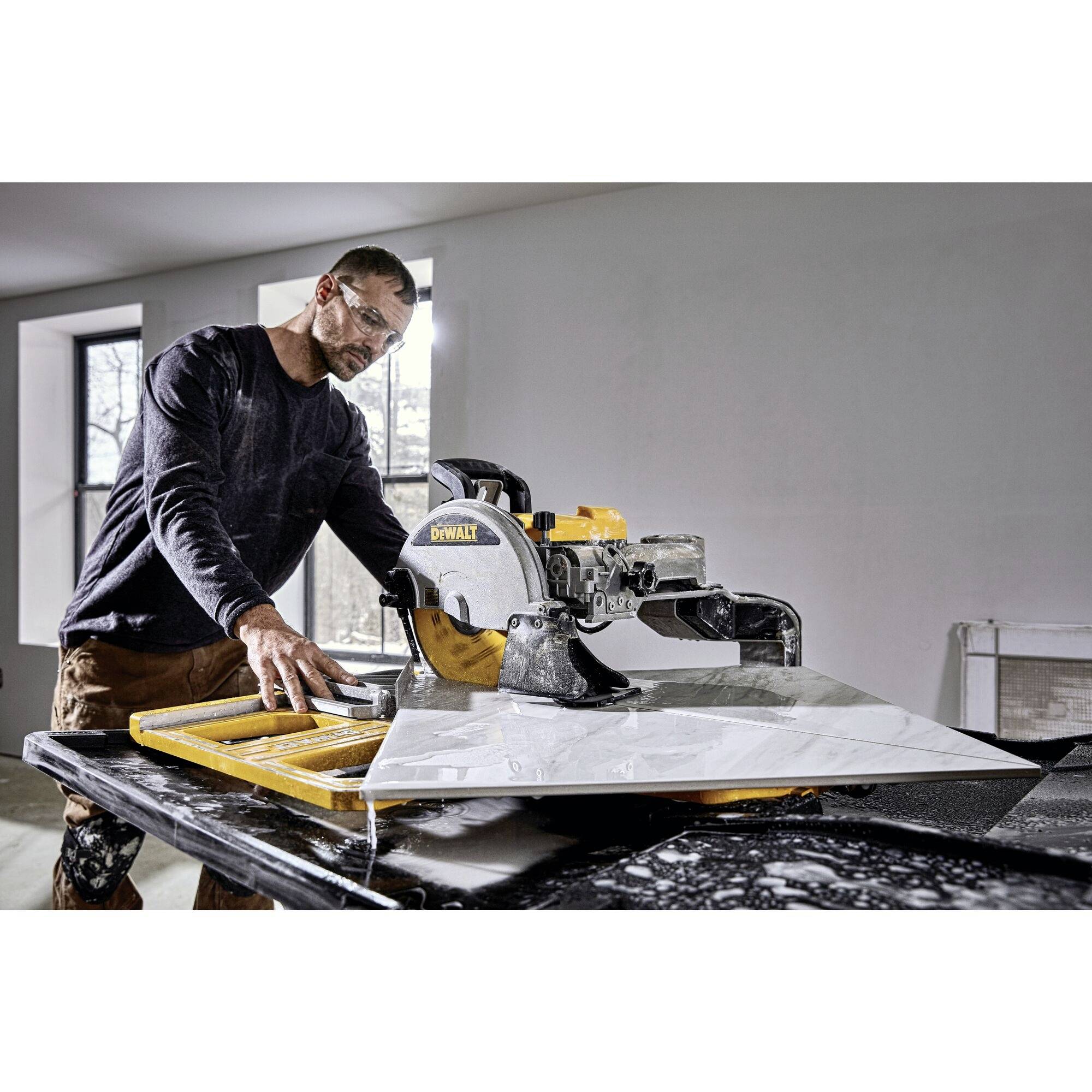 A man is cutting a large board with an electric saw. He is wearing safety glasses and is focused on his work.