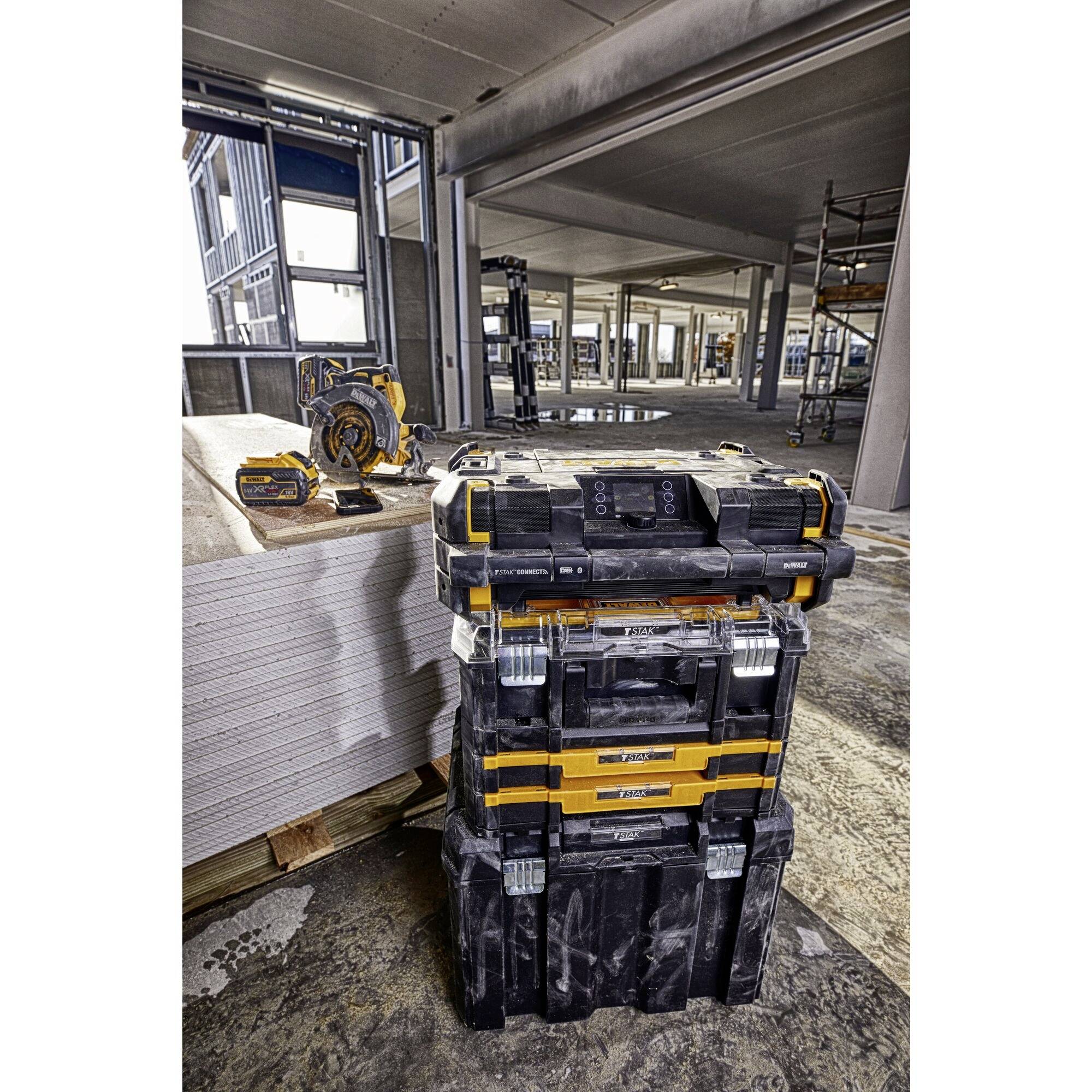 Workshop with stacked toolboxes, a saw and plasterboard sheets. Structural building elements visible in the background.