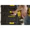 A person is reaching for a yellow handle of a stackable black toolbox by the brand 'Stanley' with yellow details.