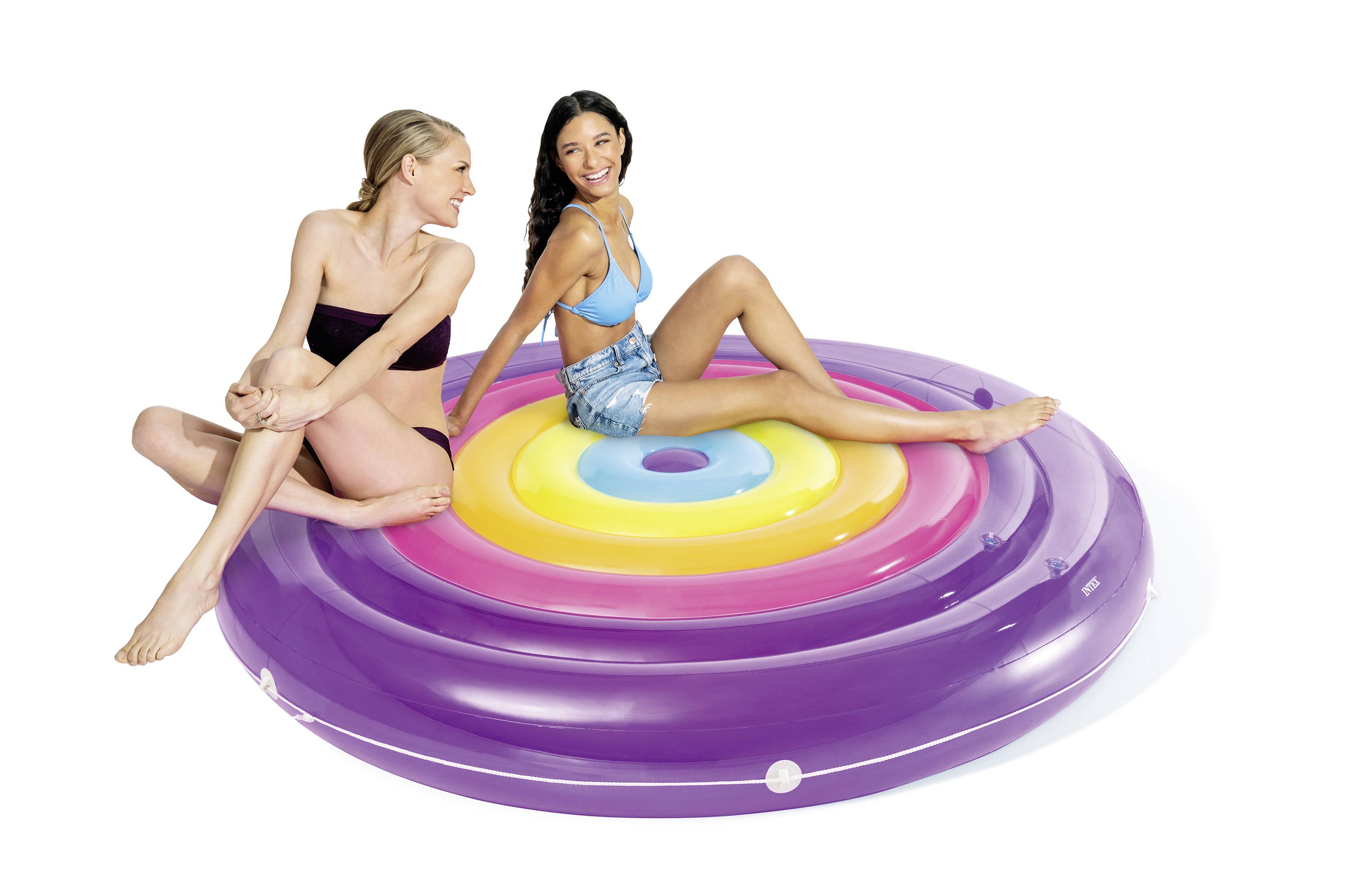 Two people are sitting on a large, round inflatable mattress in rainbow colours. They are smiling and enjoying their leisure time.