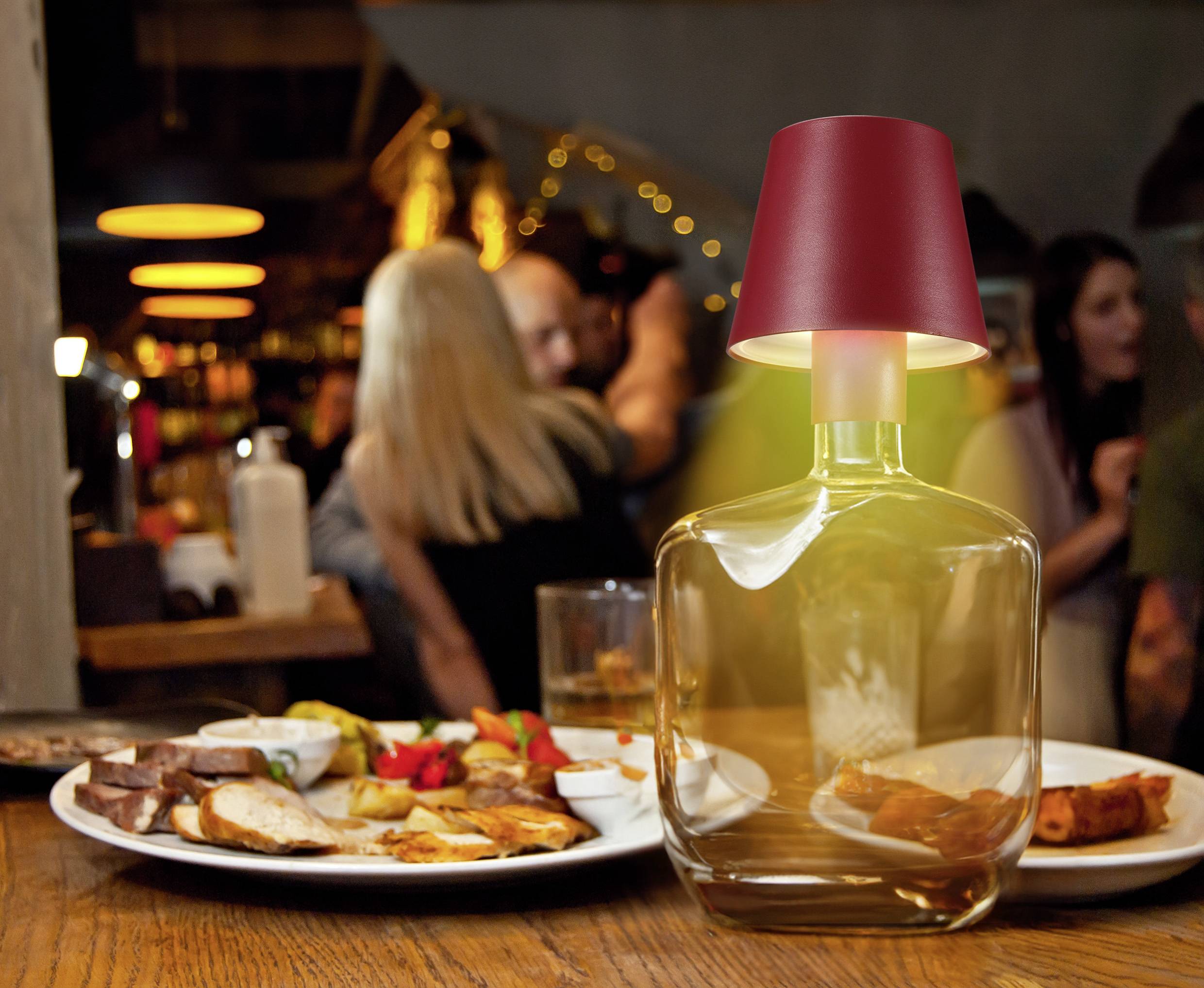 People chatting in a restaurant. In the foreground, a decorative lamp sits on a table with a plate full of food.