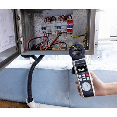 'Hand holding digital multimeter displaying 0.489 near electrical panel with visible wires and circuit breakers, blue wall background.'