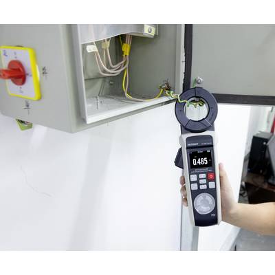 A person uses a clamp meter to measure the current flowing through a wire in an electrical panel, showing a reading of 0.485.