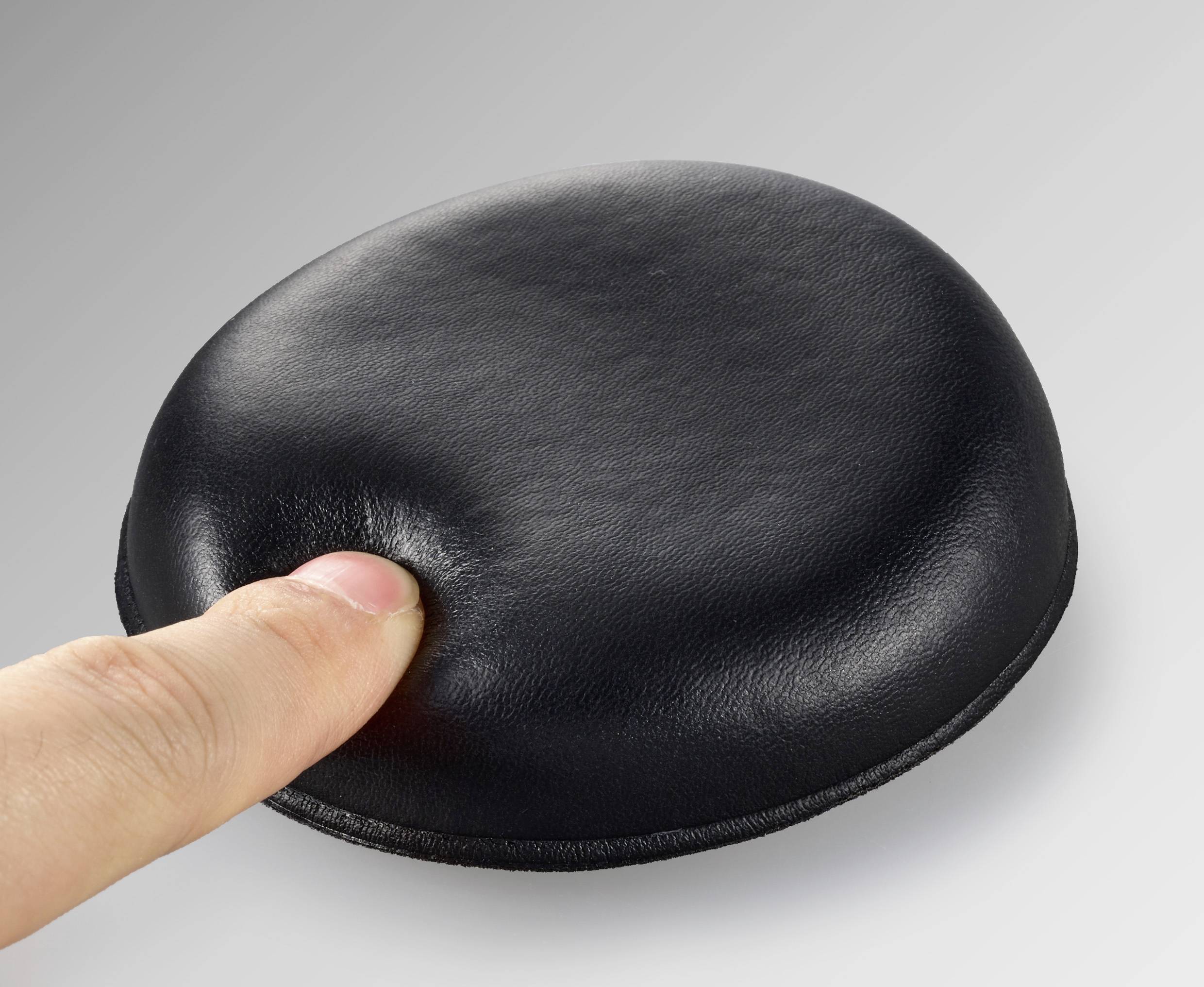 'A finger presses onto a soft, black cushion on a grey surface.'
