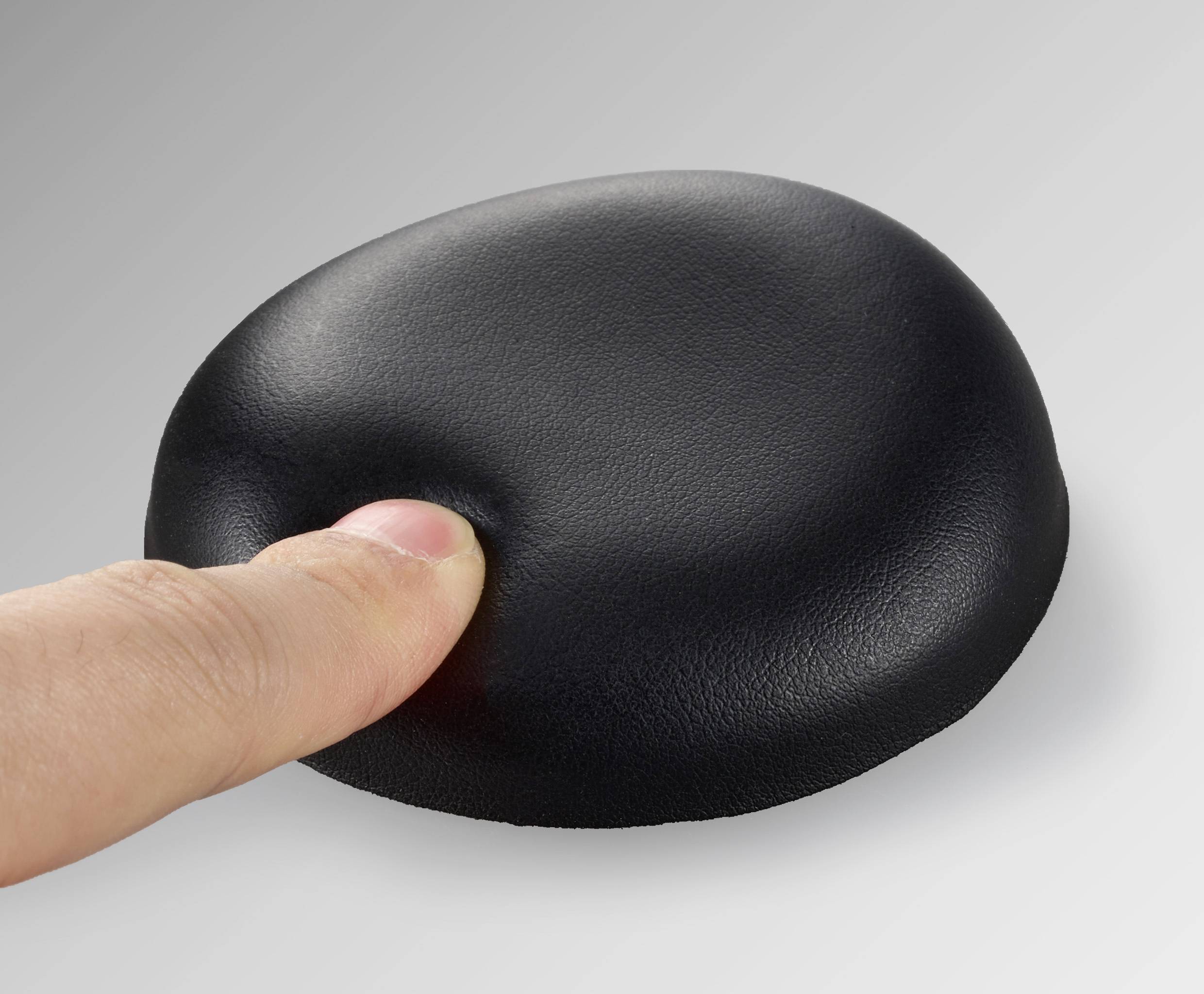 A finger presses down on a black, soft cushion, which yields slightly and creates an indentation.
