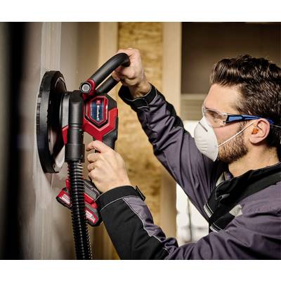 A man wearing safety glasses and a mask is grinding a wall with an electric grinding machine.