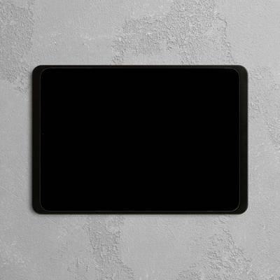 A black tablet with a switched-off screen lies on a grey, textured surface.