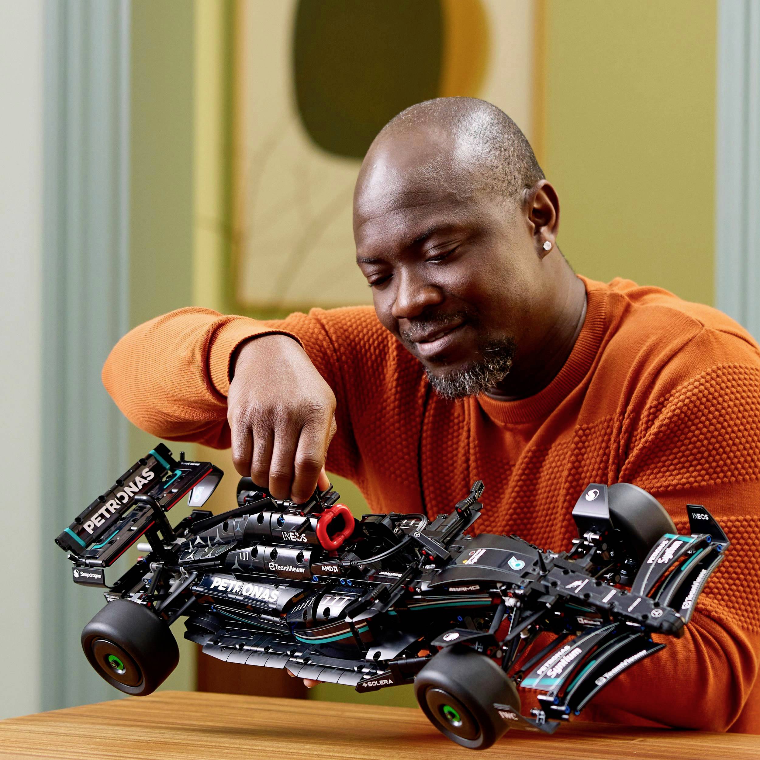 A person in an orange jumper holds a detailed model of a Formula 1 car in their hands and studies it with interest.