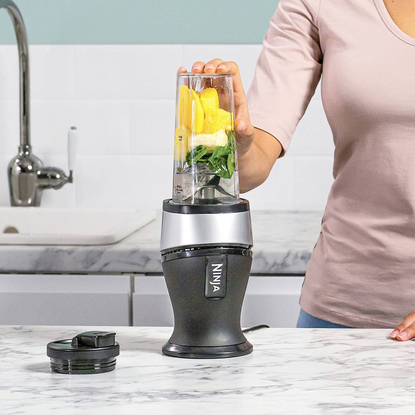A person is blending a smoothie of spinach, mango and banana in a blender on a kitchen worktop.