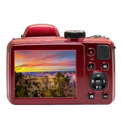 A red digital camera displays an image on its screen of a colourful sunset over a canyon with trees in the foreground.