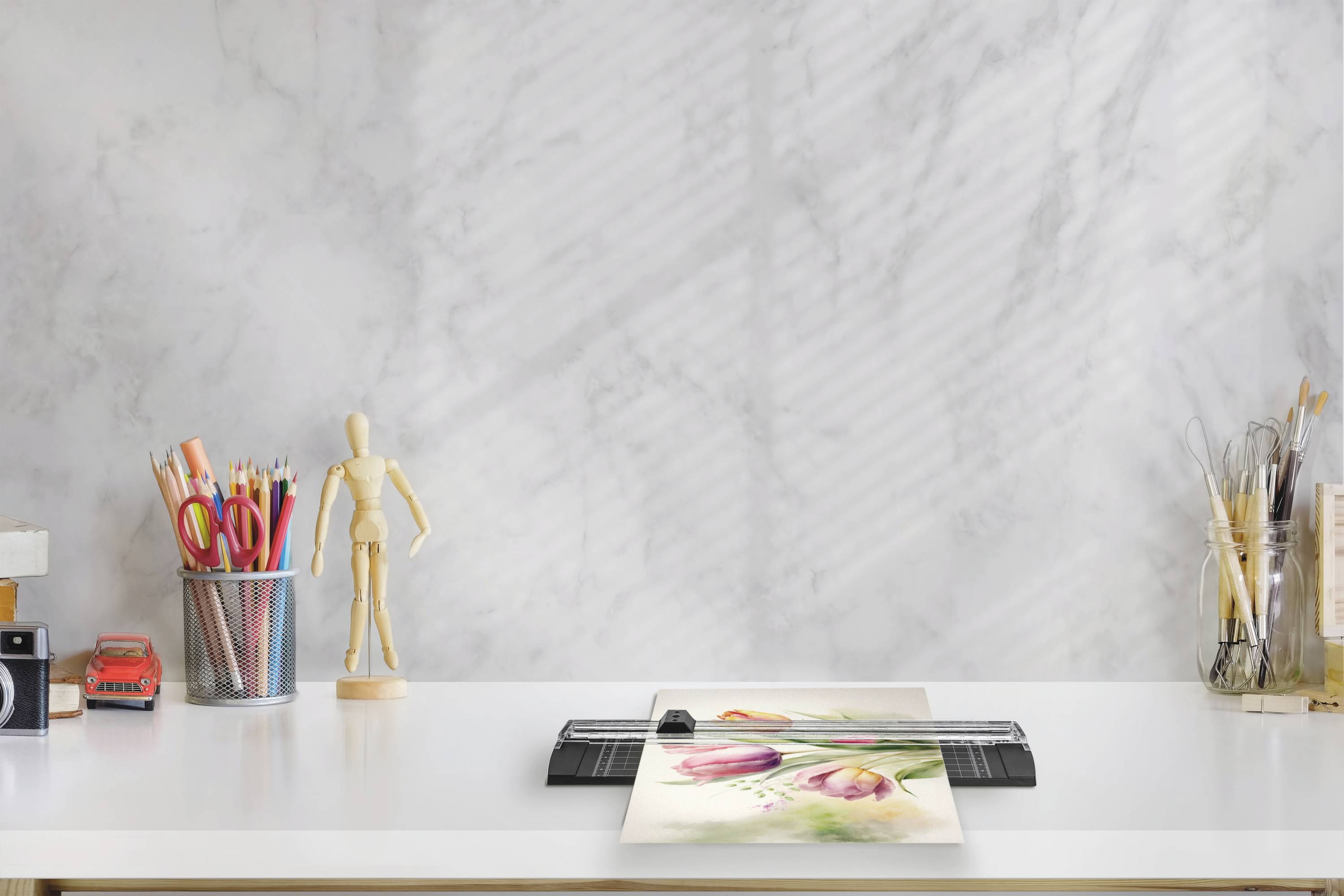 A desk with a printer in the centre, printing an image of tulips. Next to it are pen holders and a wooden figurine.