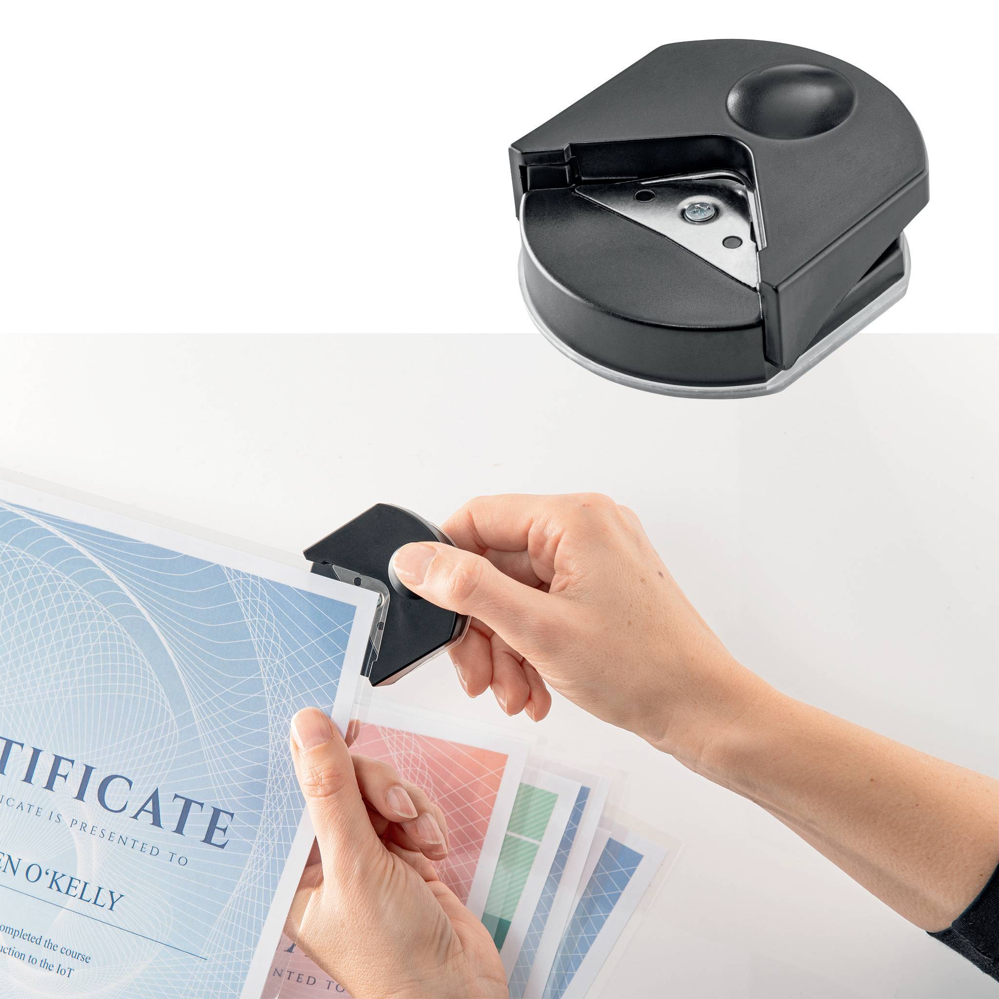 A hand is using a corner rounder to smooth the edges of a certificate. Several stacks of paper are visible.