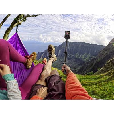 People are relaxing in a hammock with a mountain view. One person is holding a camera to capture the scenery.