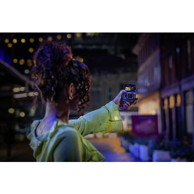A woman with curly hair photographs herself at night in a lit-up city, camera in hand.