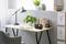 A minimalist desk with a lamp, plants, books and a radio. Next to it stands a grey chair.