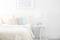 Bright bedroom with a white bed, colourful cushions and a small table with a white radio placed on it. Vibrant picture on the wall.