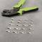 A green crimping pliers lies beside 16 cable lugs on a grey surface.