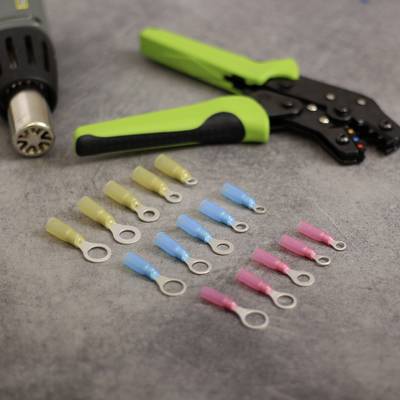 A heat gun and crimping pliers on a table. Nine cable connectors in three colours (yellow, blue, pink) are arranged beside them.