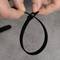 Hands securing a black cable tie against a grey background.