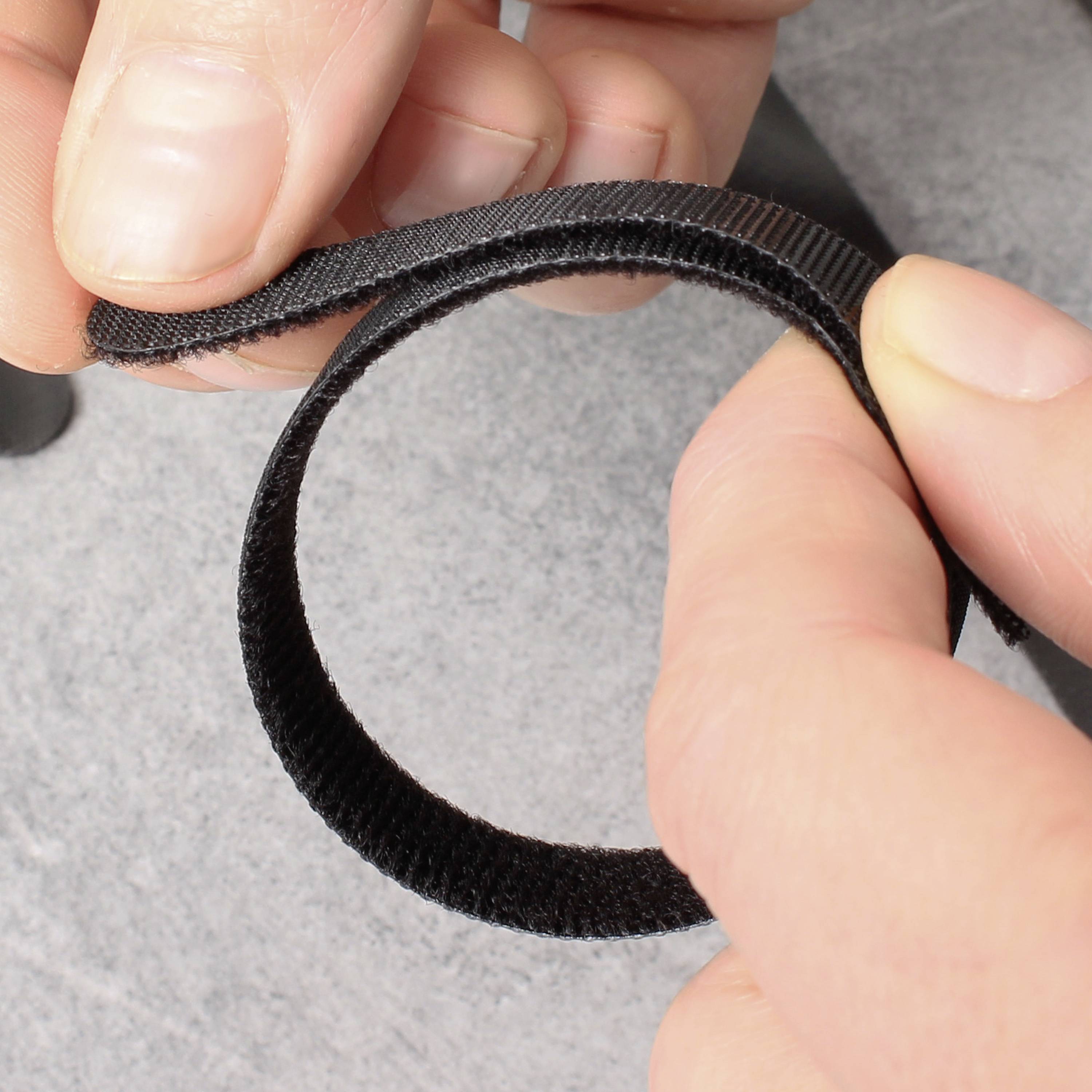 A person is holding a piece of hook and loop fastener (Velcro) with both hands. The fastener is half-open, displaying its hook and loop sides.