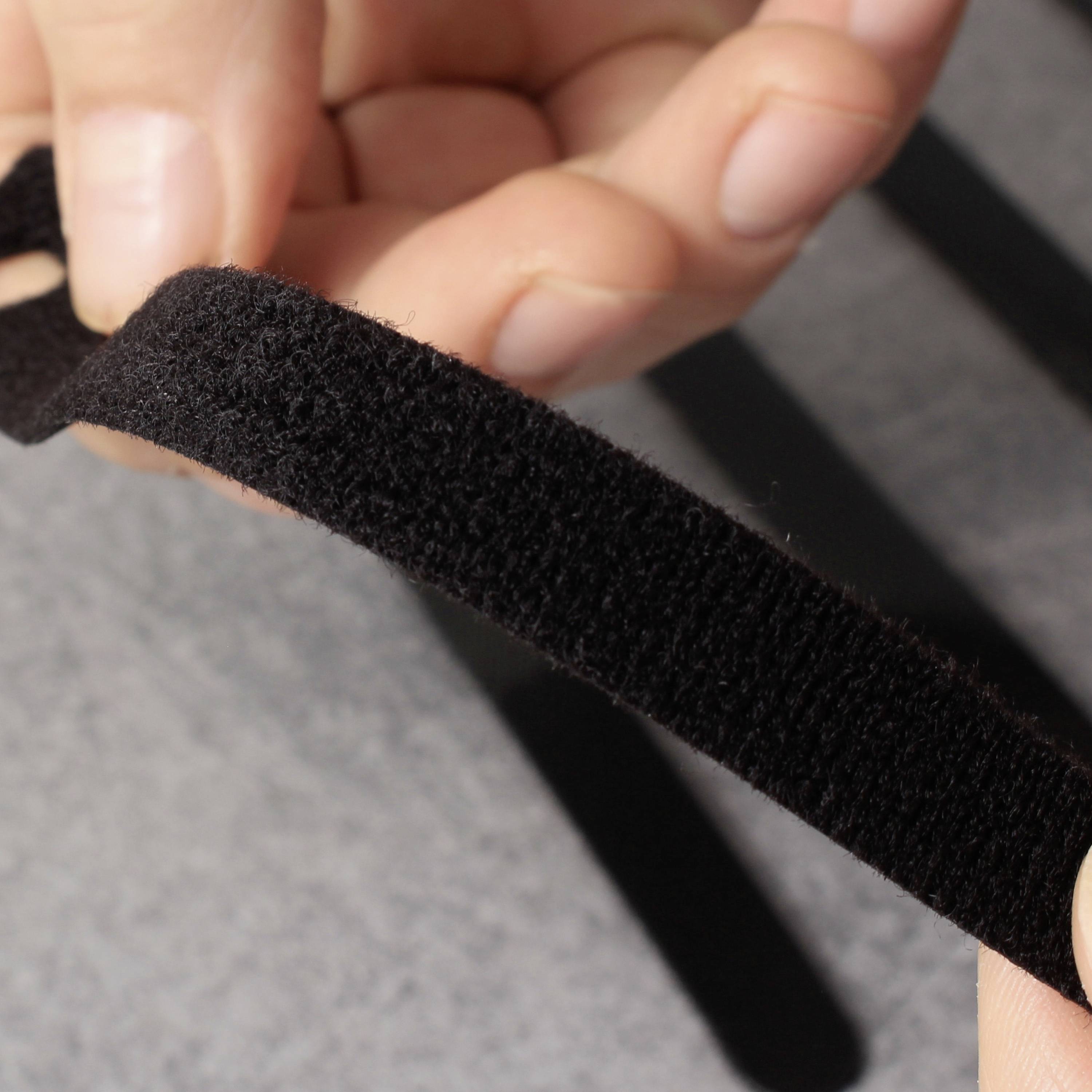 A hand holds an opened black hook-and-loop fastener against a dark background.
