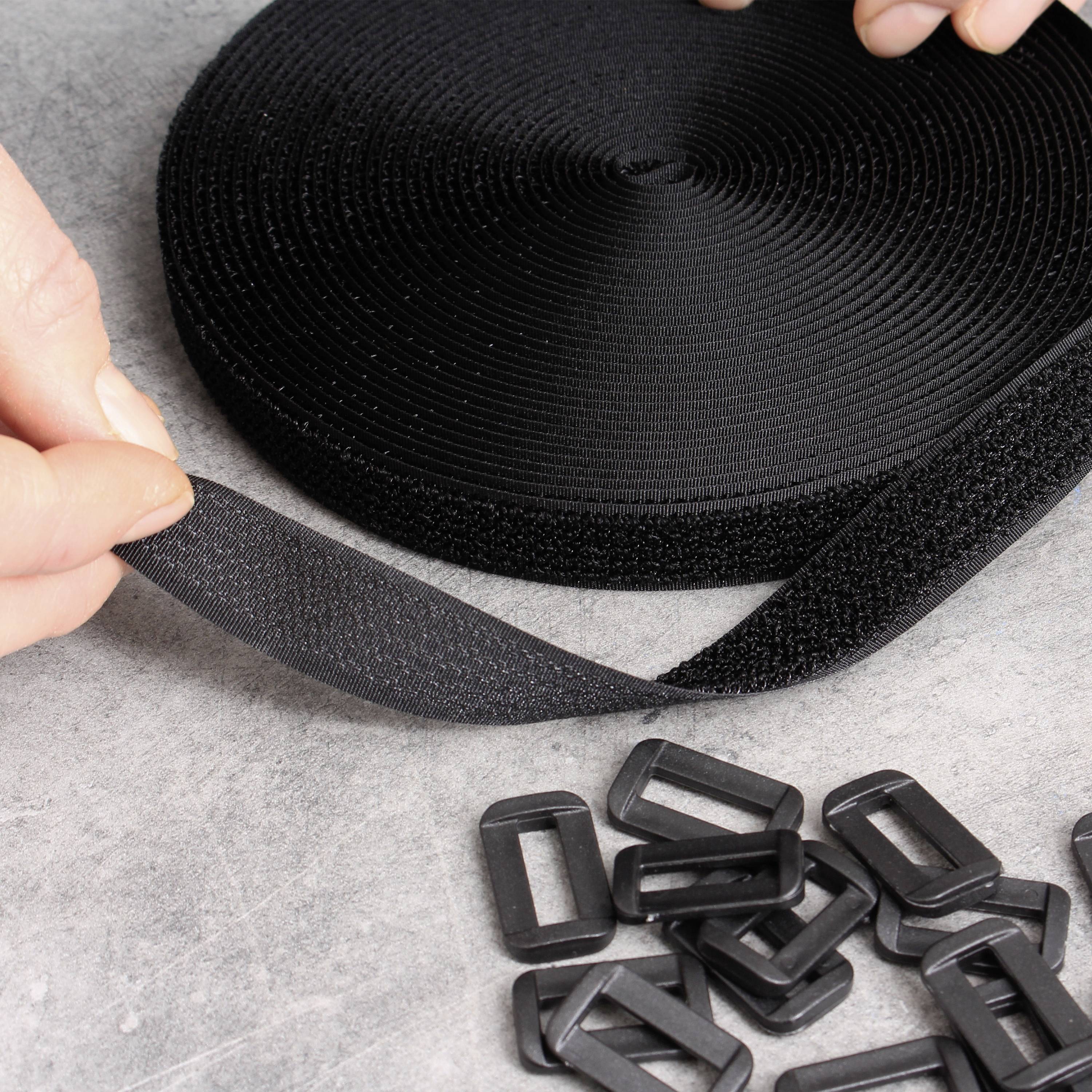 Black hook and loop tape rolled out next to several black plastic buckles, hand holding the end of the tape. Suitable for fastening purposes.