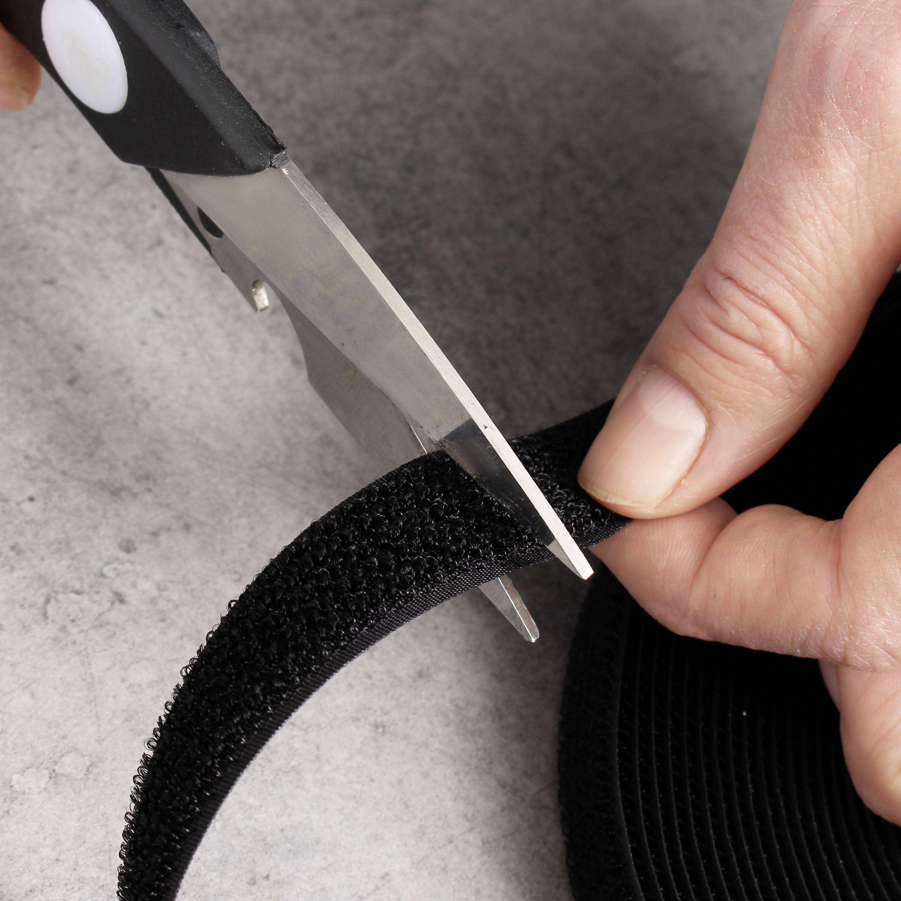 A hand cuts a hook and loop fastener strip with scissors on a grey surface.