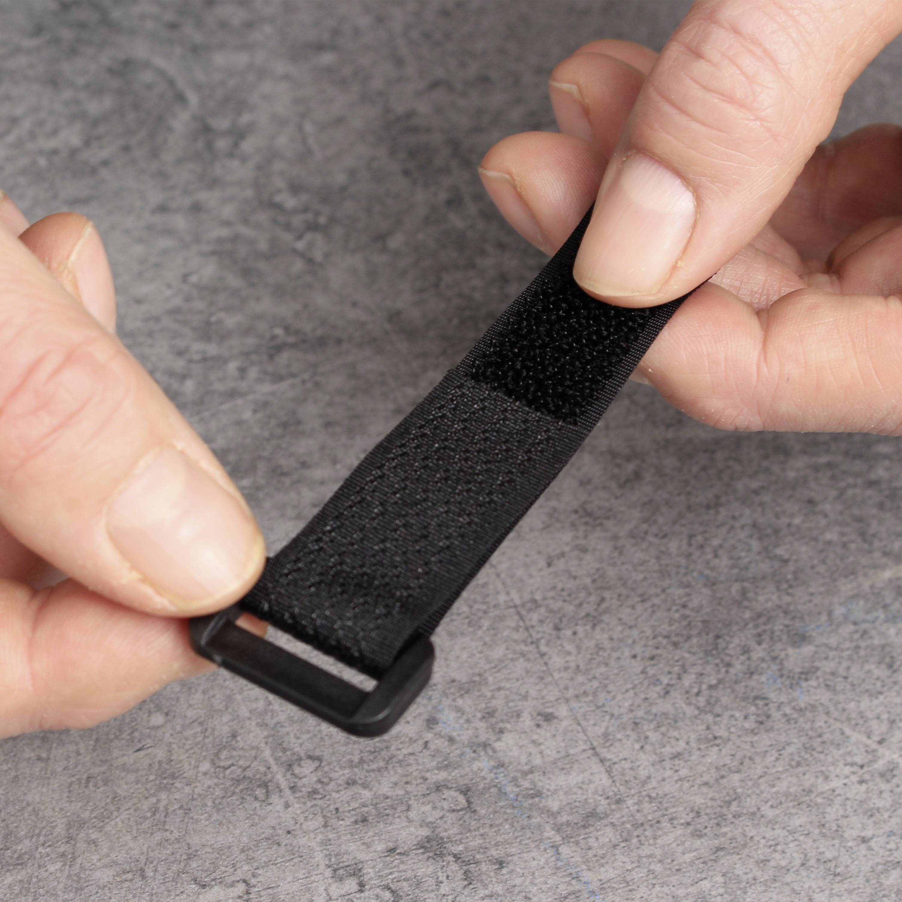 A hand pulls tightly on a black hook and loop fastener strip, which may be used for securing or organising objects.