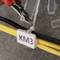A person is cutting a cable tie from cables labelled 'KM3' using a pair of pliers.