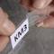 Close-up of two hands holding a small plastic holder with a white paper strip inside. The paper reads 'KM3'.