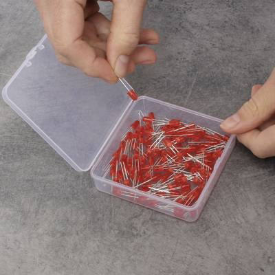 A hand holds a red LED, while another hand opens a box containing numerous red LEDs. The LEDs are loose inside the box.