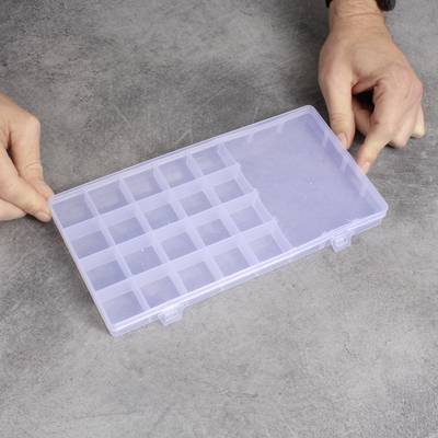 A person is holding a transparent plastic box with multiple small compartments, suitable for storing small parts.