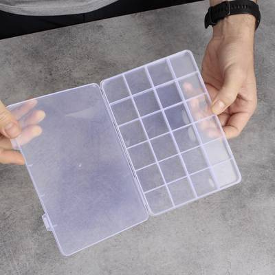 A person opens an empty transparent sorting box with multiple compartments on a table.