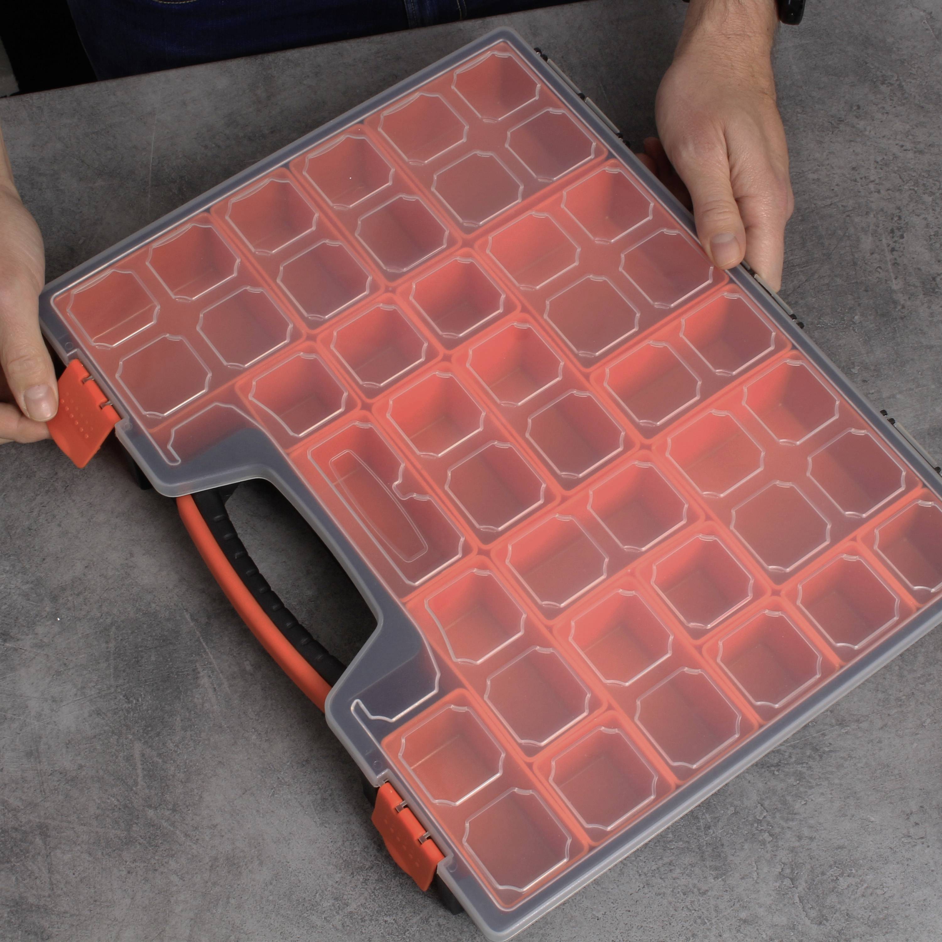 A person is holding a transparent case with numerous small, red compartments, suitable for storing small items.