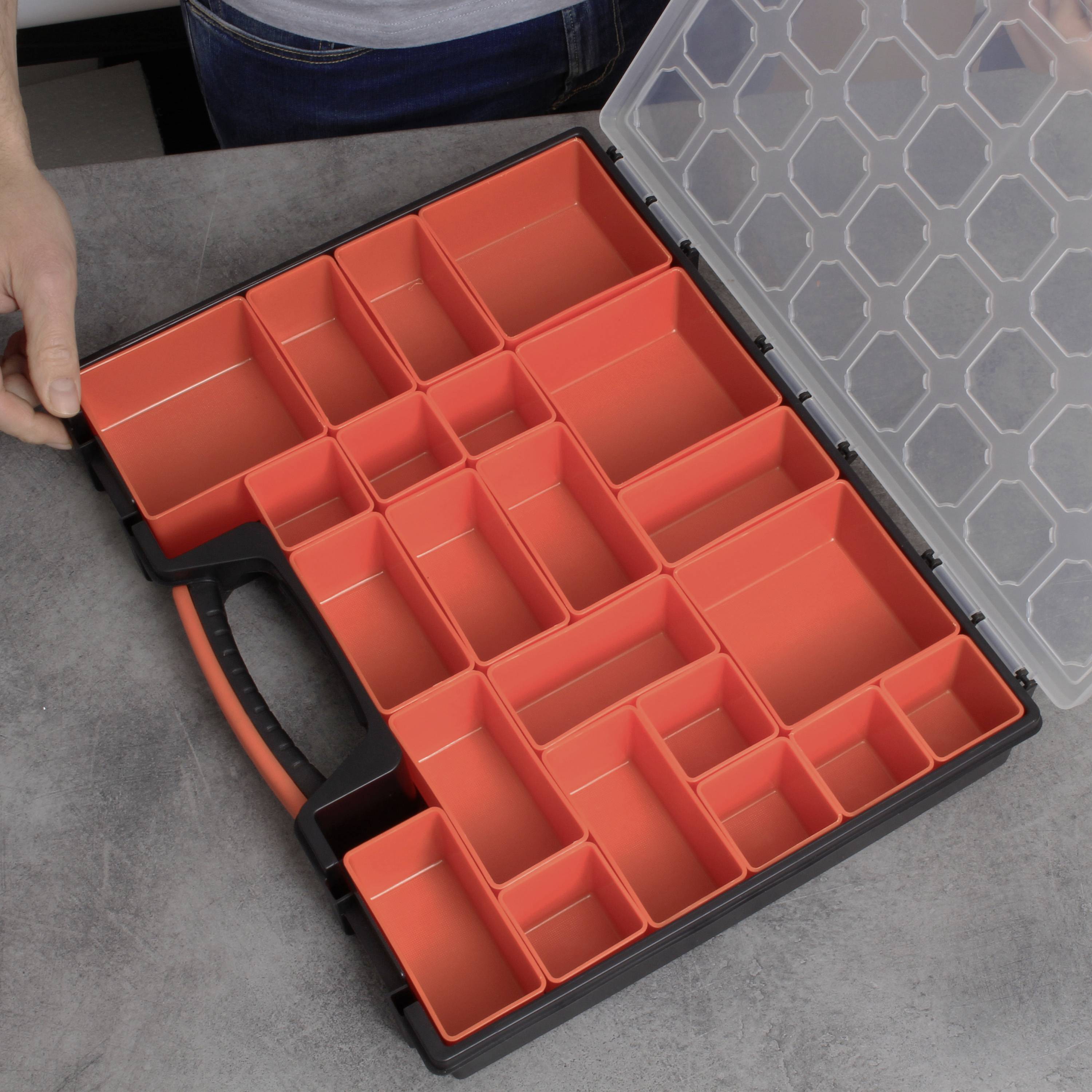 A person is holding an open plastic compartment box with numerous red compartments. The box is resting on a grey table.