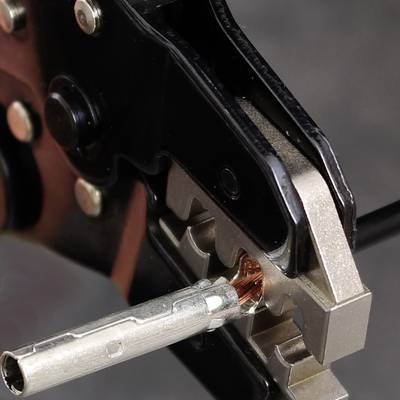 Close-up of a crimping tool connecting a cable end with a metal terminal.