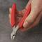 A hand is holding a small side cutters with red handles, ready to cut something.