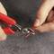 A person is cutting a red cable with red pliers on a grey surface. Hands focused, demonstrating precise work.
