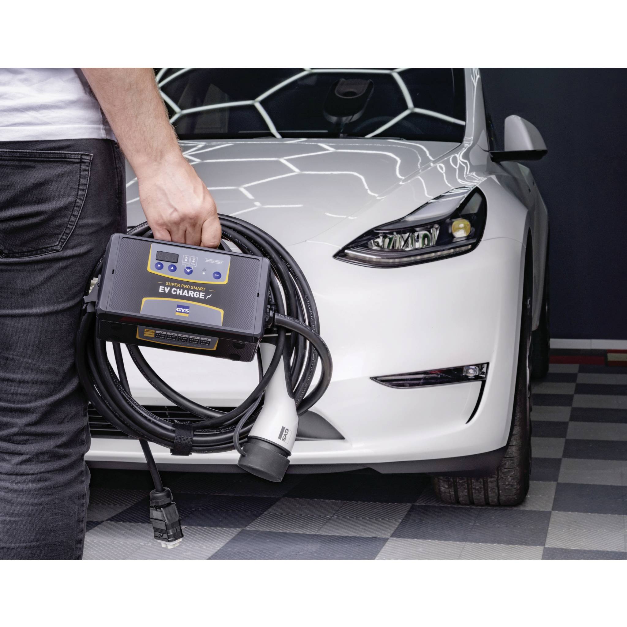 A person is holding a charging cable next to a white electric car parked in a garage. The focus is on sustainable mobility.